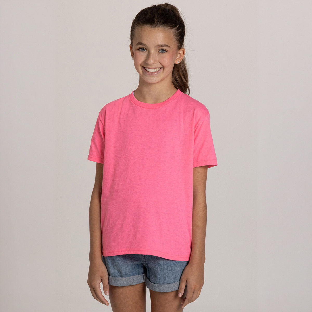 A young girl smiling while wearing a neon pink Jerzees Classics Youth T-Shirt.