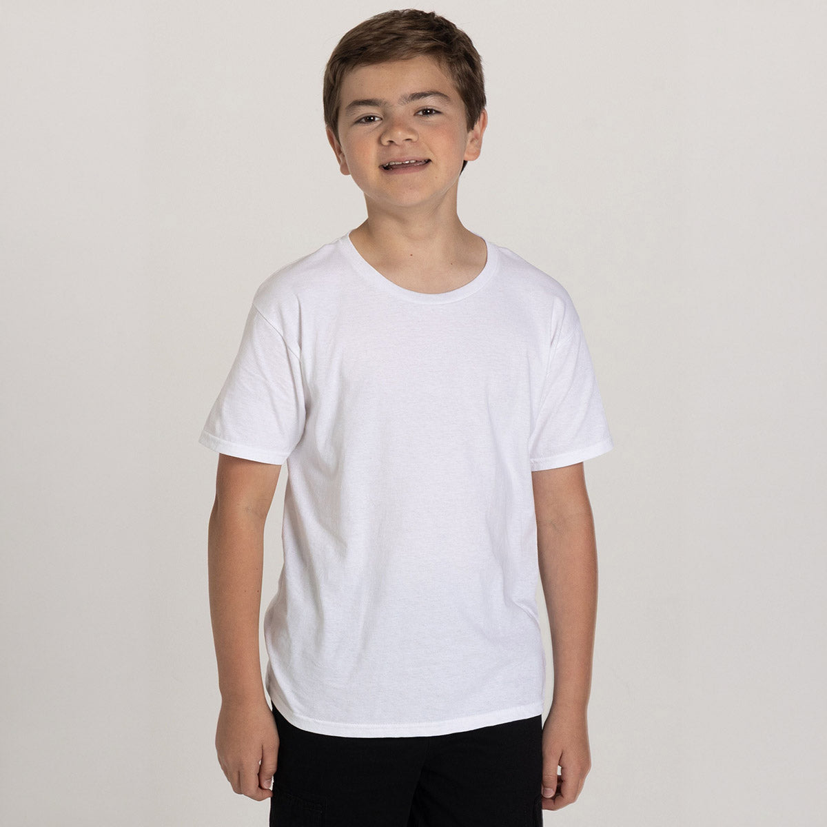 A young boy wearing a white Jerzees Classics Youth T-Shirt standing against a plain light gray background.