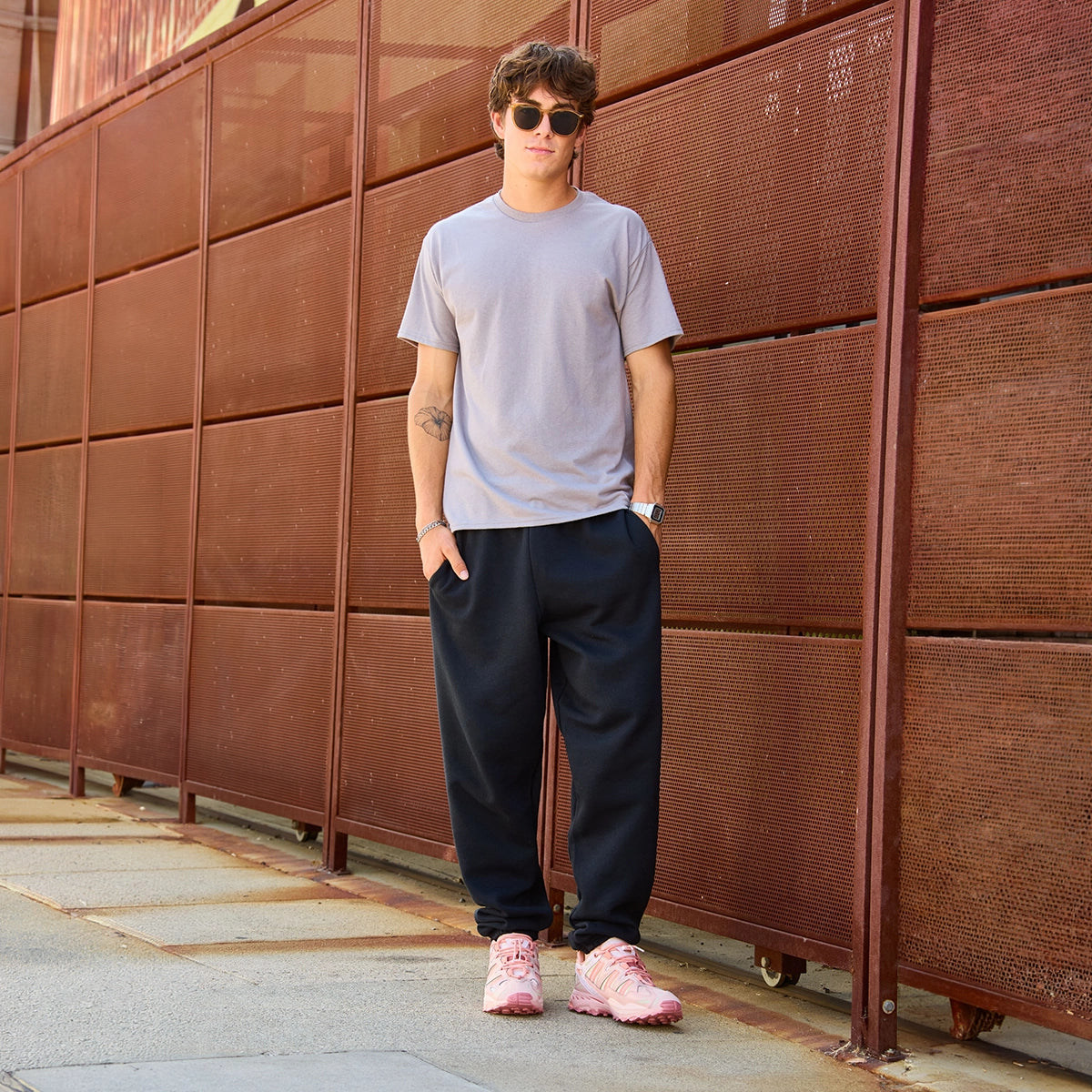 A young man wearing Jerzees Super Sweats NuBlend black sweatpants, a gray t-shirt, and pink athletic sneakers.