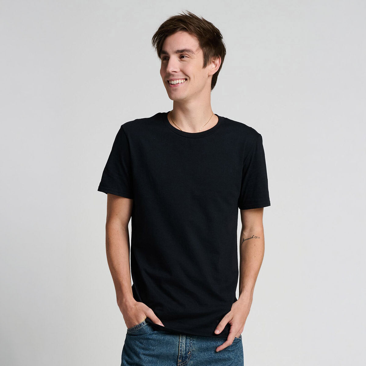 Smiling man modeling a black Jerzees Premium Combed Ring-Spun Cotton Unisex T-Shirt against a light gray background.