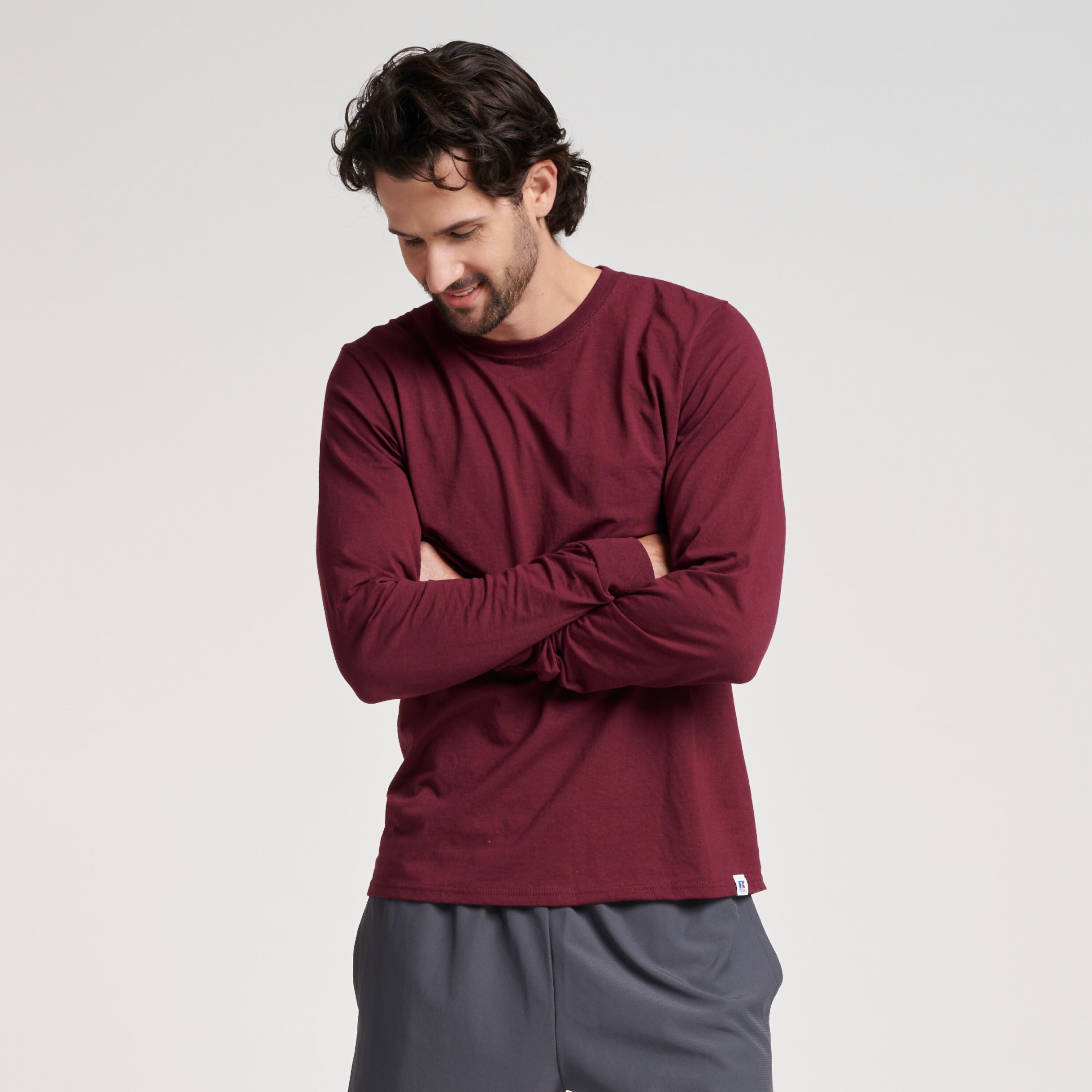 Man wearing a maroon Russell Athletic DRI-POWER® CVC Performance unisex long-sleeve t-shirt with arms crossed.
