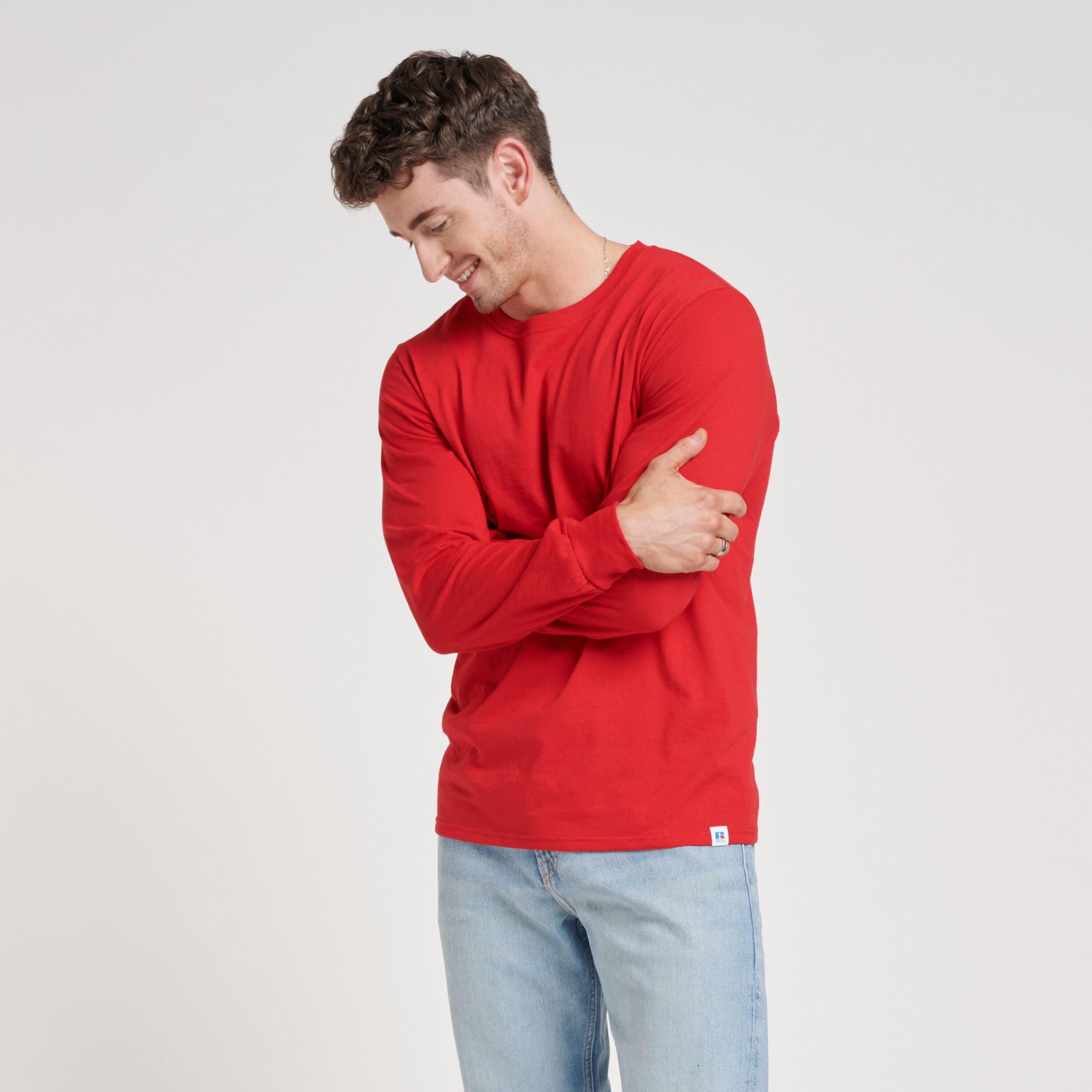A model wearing a True Red Russell Athletic DRI-POWER® CVC Performance Unisex Long-Sleeve T-Shirt with arms crossed.