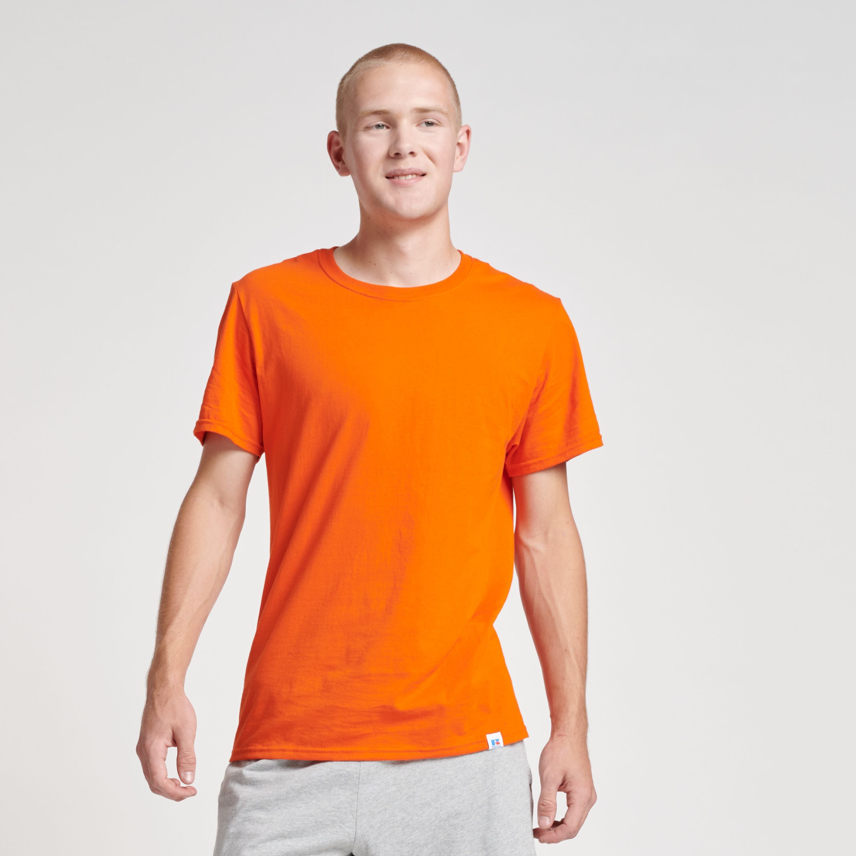 A man wearing a Russell Athletic DRI-POWER CVC Performance T-Shirt in burnt orange with grey athletic shorts.