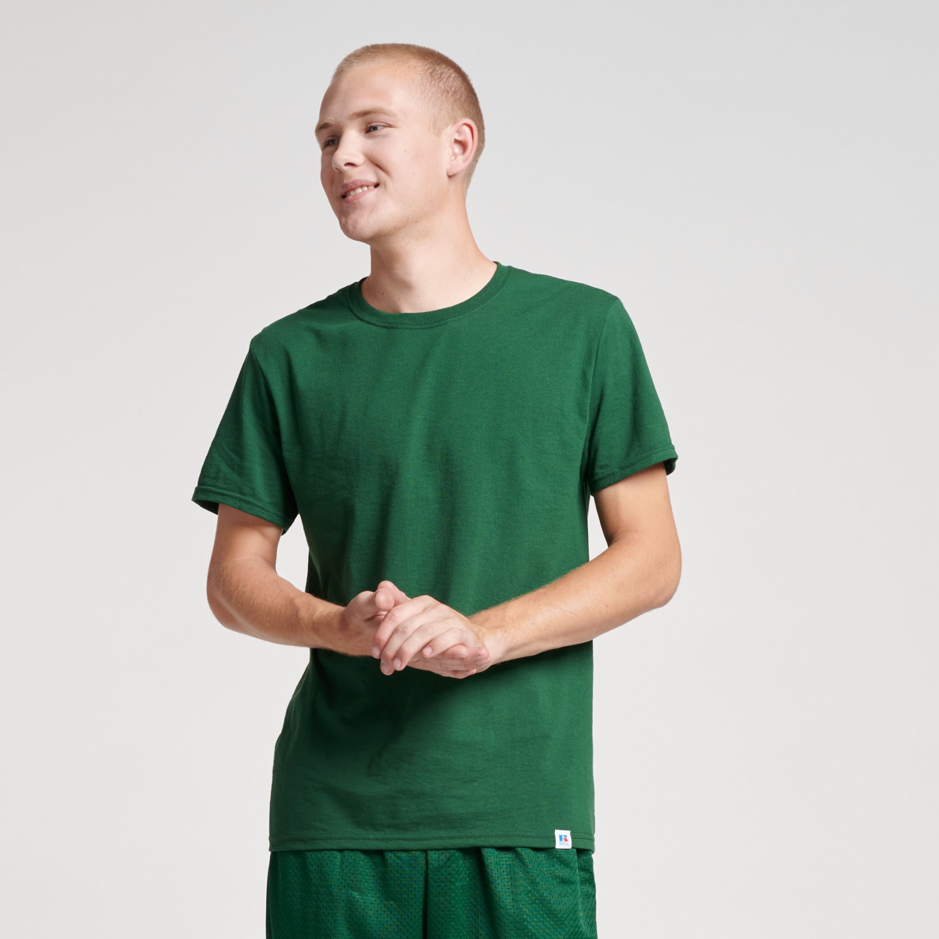 A person wearing a dark green Russell Athletic DRI-POWER CVC Performance Unisex T-Shirt against a light background.