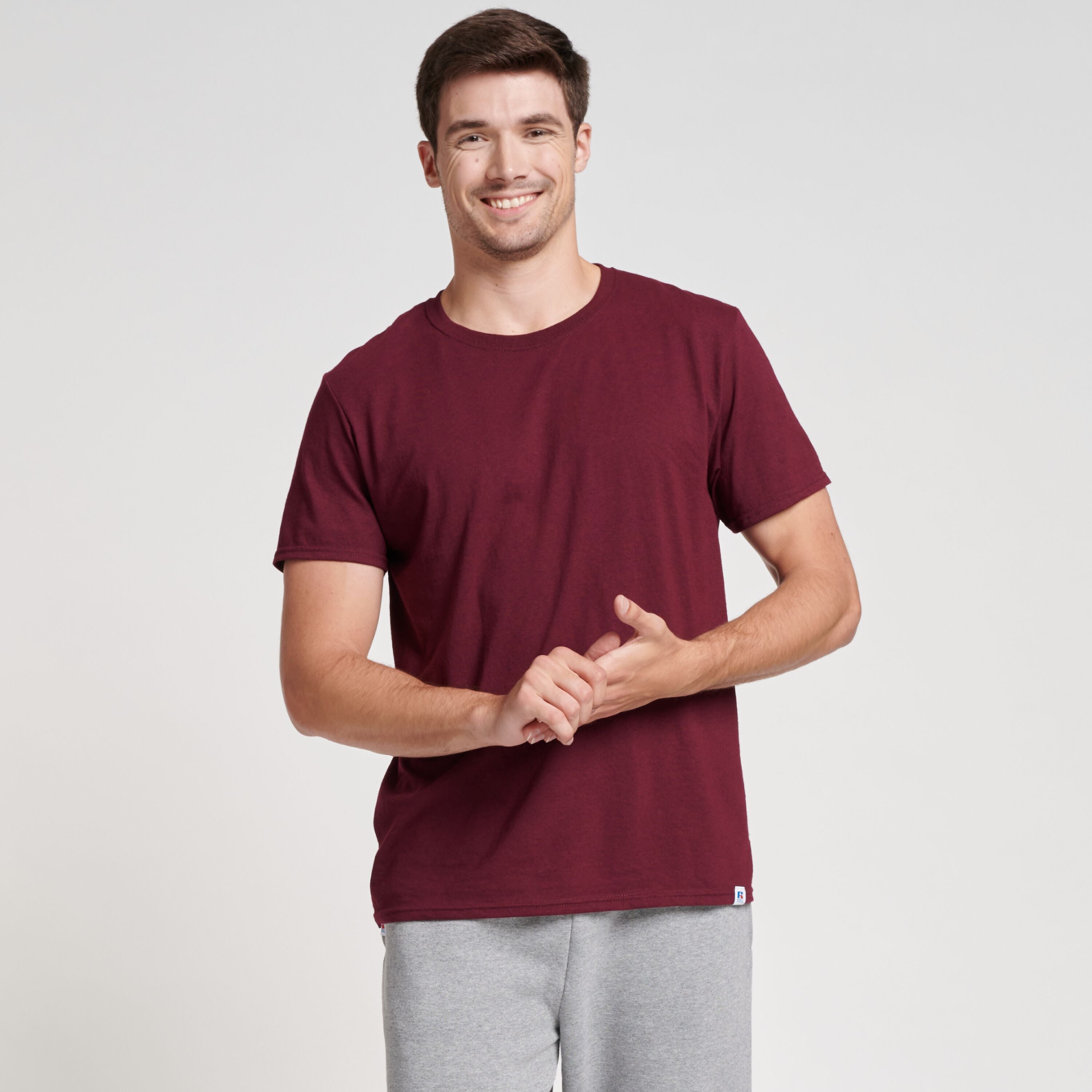 A man wearing a maroon Russell Athletic DRI-POWER CVC Performance unisex short-sleeve T-shirt and grey sweatpants.