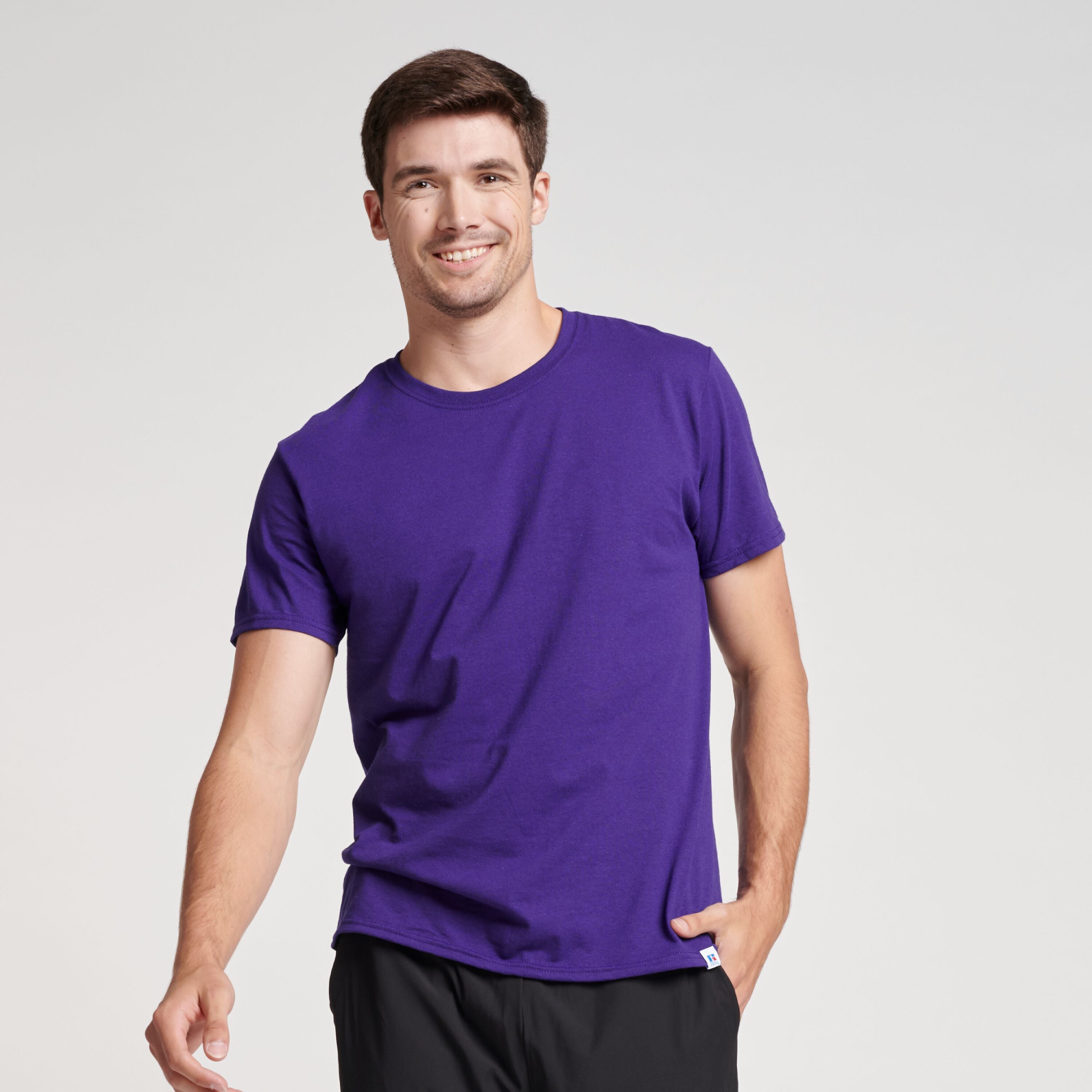 A male model wearing a purple Russell Athletic DRI-POWER CVC Performance unisex short-sleeve T-shirt.