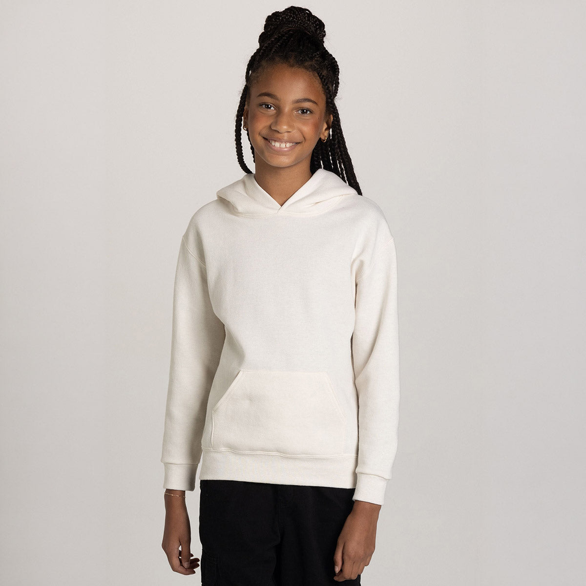 A young girl wearing a Sweet Cream Heather Jerzees NuBlend® Youth Hooded Sweatshirt against a plain grey background.