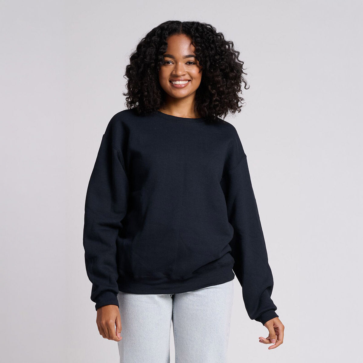 A woman smiling while wearing a black Jerzees Rugged® Unisex Sweatshirt against a light gray background.