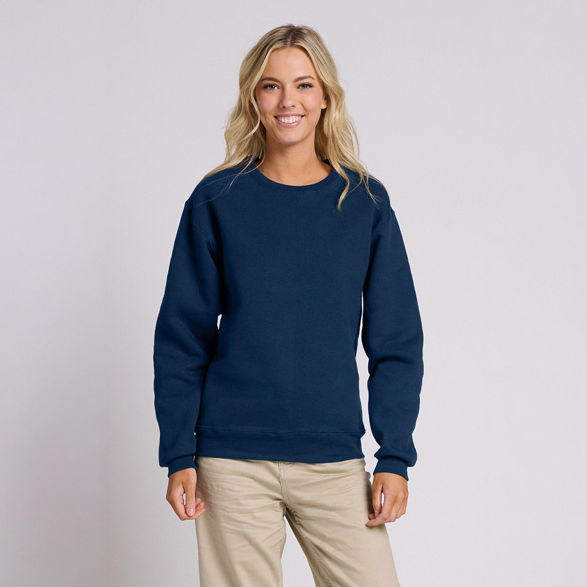Smiling blonde woman wearing a Jerzees Rugged Unisex Sweatshirt in Washed Navy against a white background.