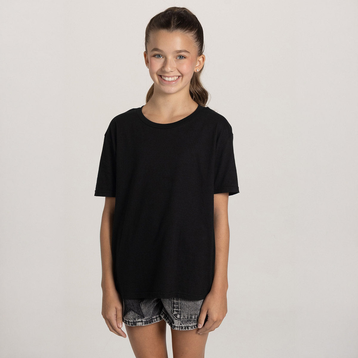 A smiling youth wearing a black Jerzees Ultimate® Ring-Spun Youth T-Shirt against a plain studio background.