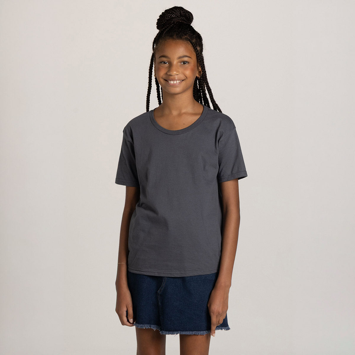 A young person wearing a charcoal grey Jerzees Ultimate® Ring-Spun Youth T-Shirt with a denim skirt.