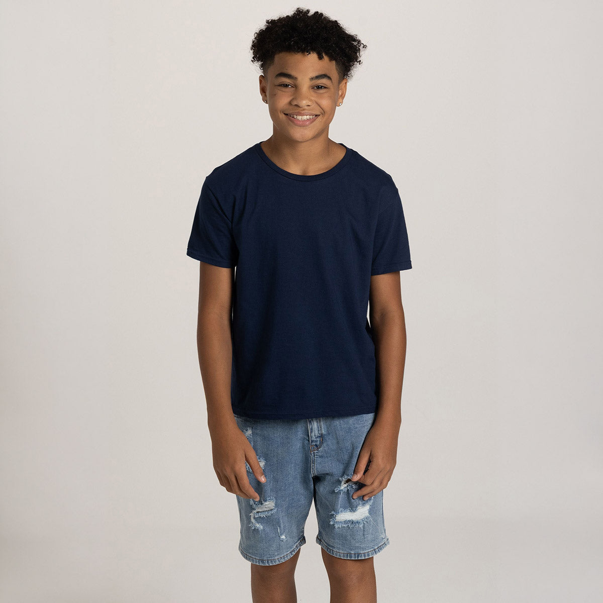A young boy wearing a Jerzees Ultimate® Ring-Spun Youth T-Shirt in J. Navy paired with distressed denim shorts.