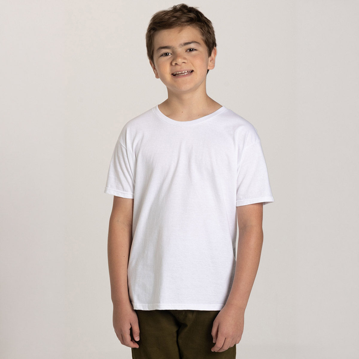 A young boy wearing a white Jerzees Ultimate® Ring-Spun Youth T-Shirt against a plain studio background.