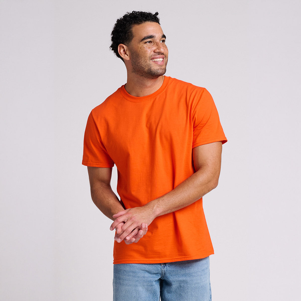 A man wearing a burnt orange Jerzees Ultimate Ring-Spun Unisex T-Shirt, standing against a light gray background.
