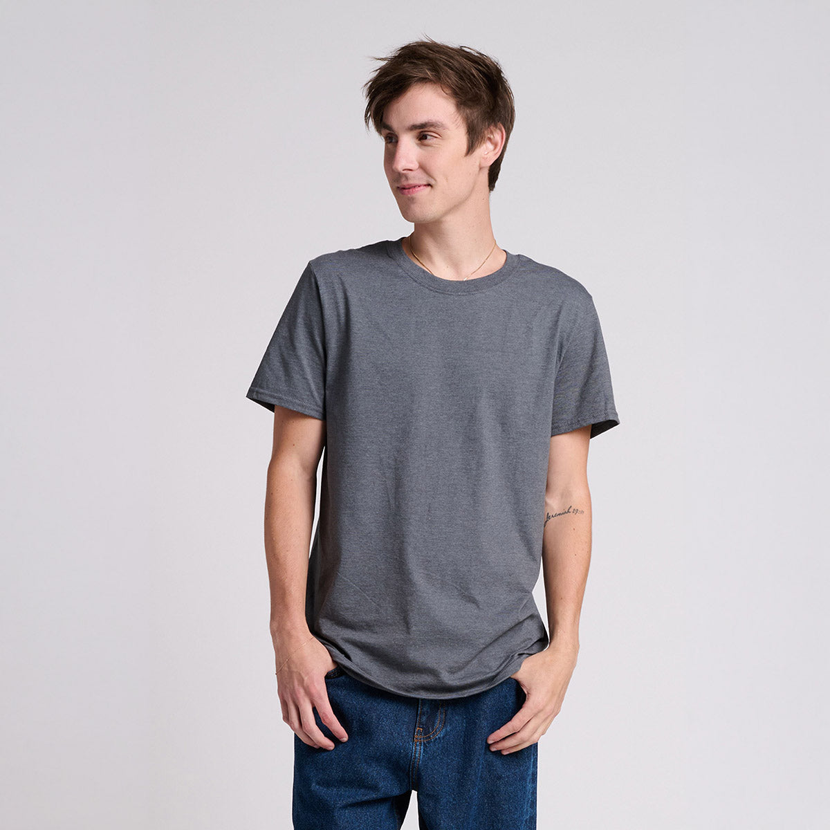 Young man wearing a charcoal heather Jerzees Ultimate Ring-Spun Unisex T-Shirt against a grey background.