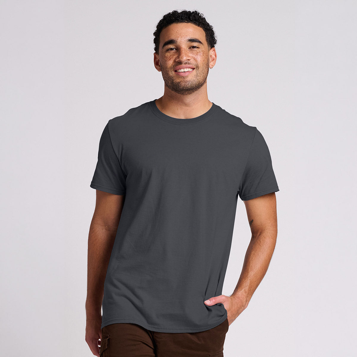 A smiling man wearing a charcoal grey Jerzees Ultimate® Ring-Spun Unisex T-Shirt against a light grey background.
