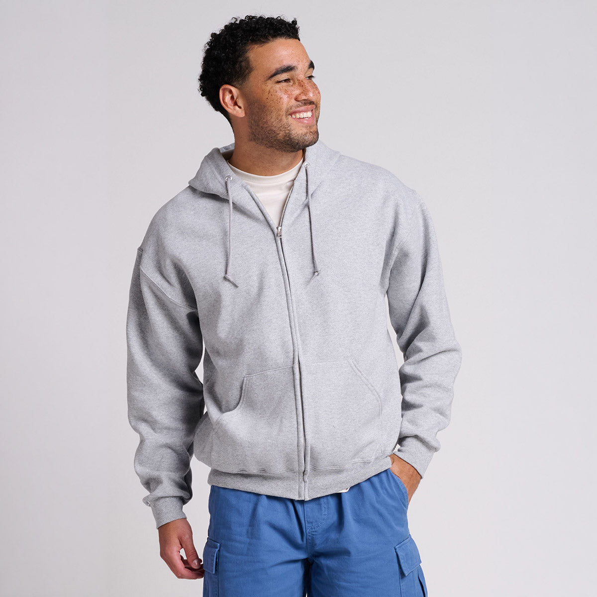 Man wearing a Jerzees Rugged Unisex Full-Zip Hooded Sweatshirt in Athletic Heather with blue cargo shorts.