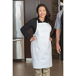 Woman wearing a white Premium Uniforms designer bib apron with pockets over a black shirt in a kitchen setting.